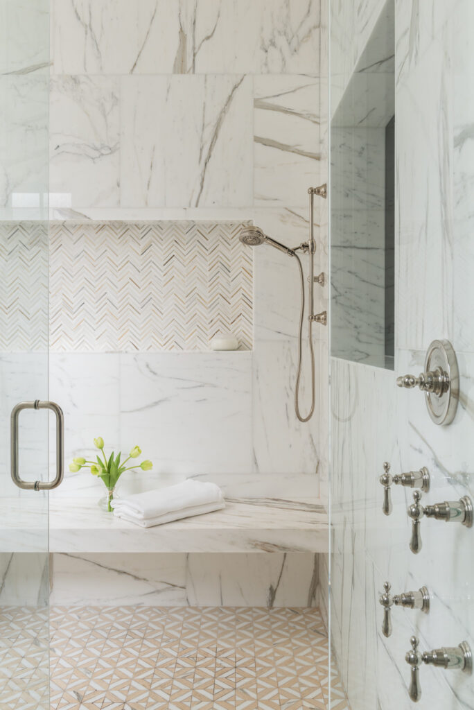 A bathroom with marble walls and floors, and a shower.